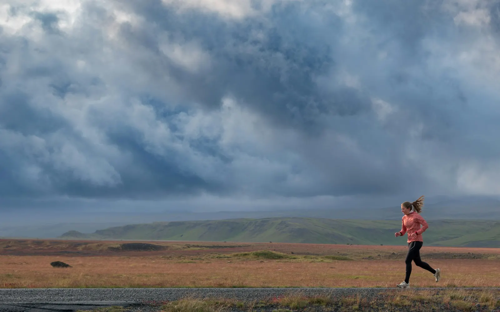 Coureuse sur un sentier balayé par le vent sous un ciel d'orage, Islande